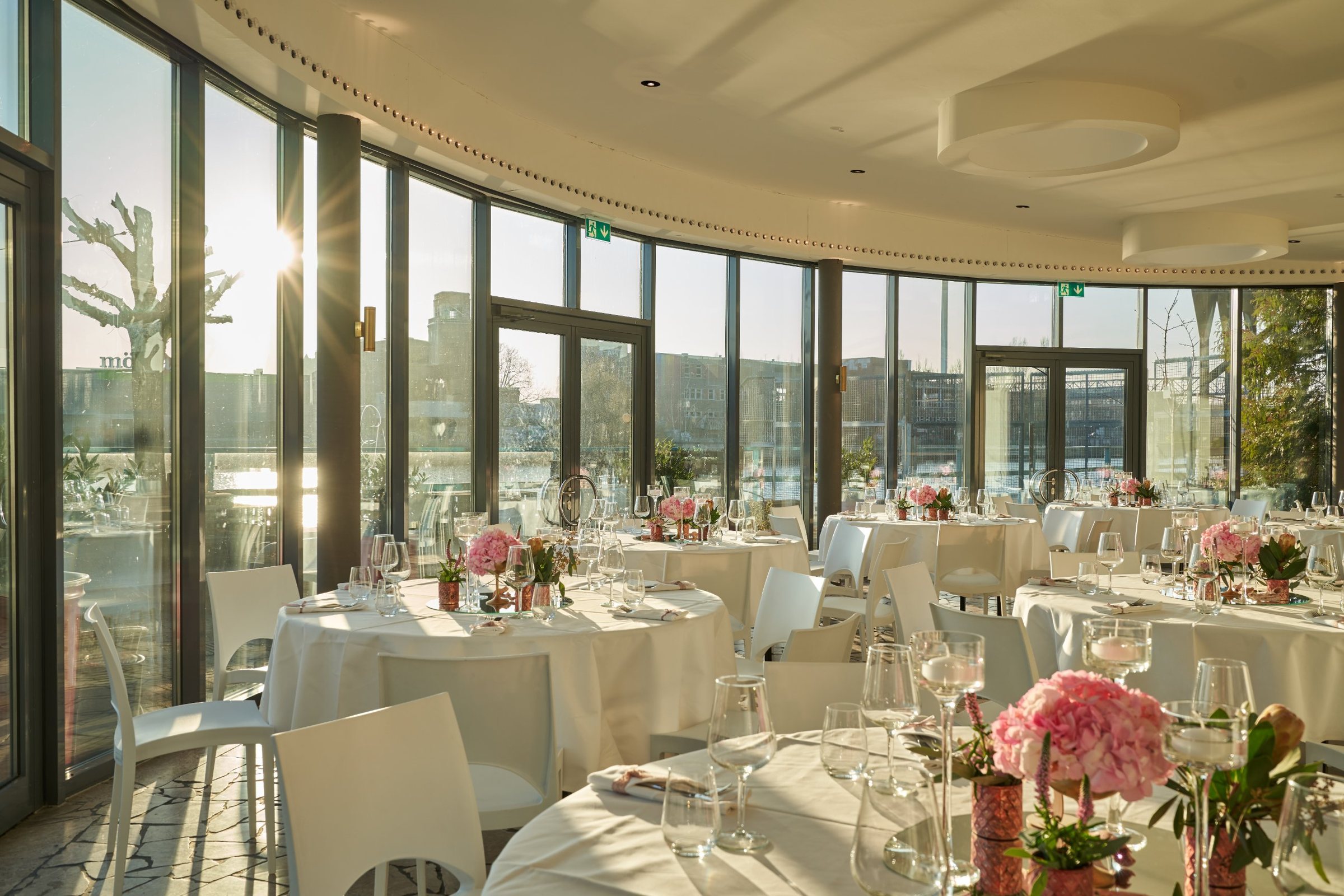 Panoramalounge im Abendlicht mit runder Glasfront und festlich gedeckten Tischen mit rosa Hortensien