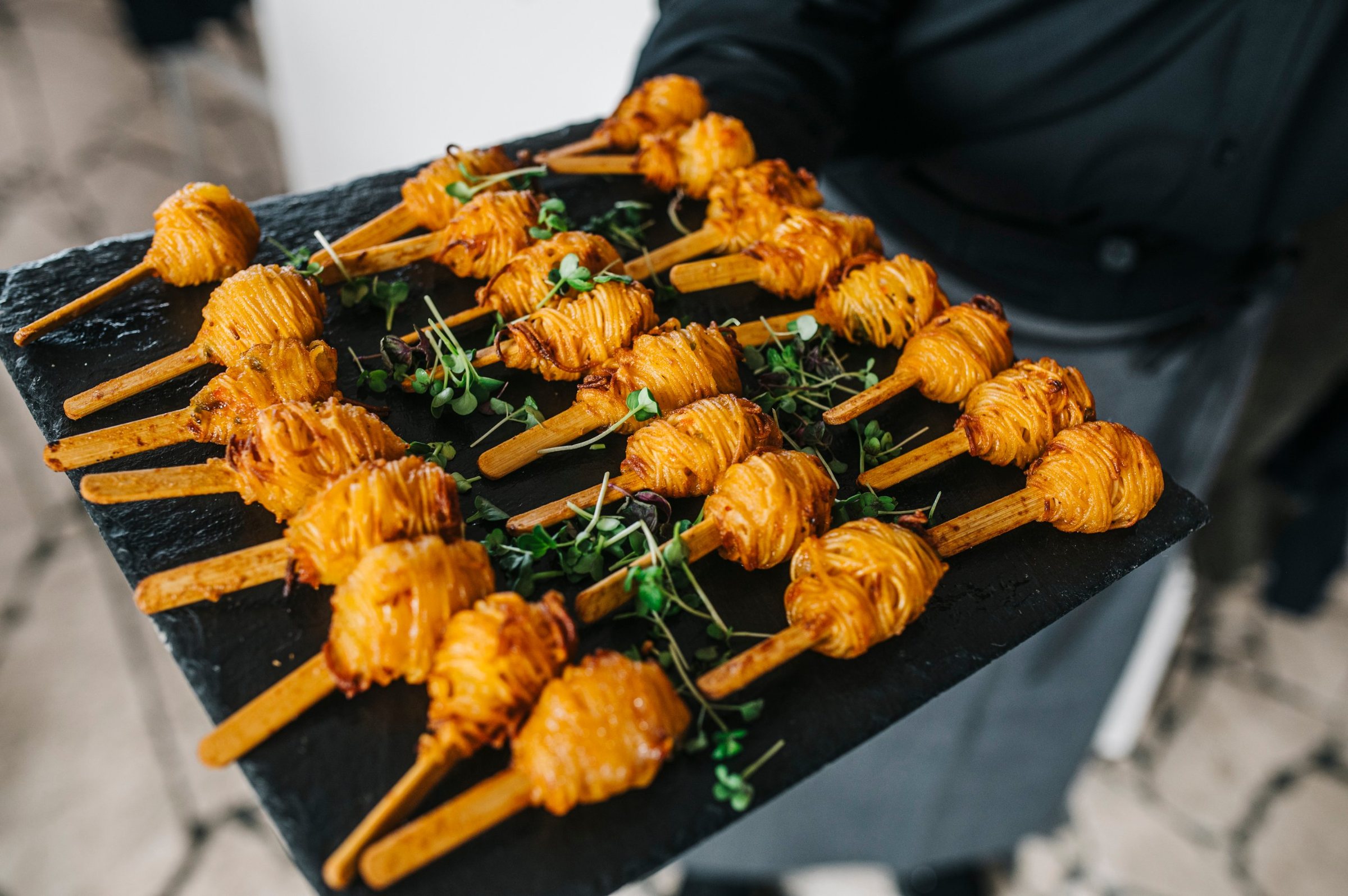 Fingerfood-Spieße mit Kresse auf einer Schieferplatte, serviert von einer Servicekraft