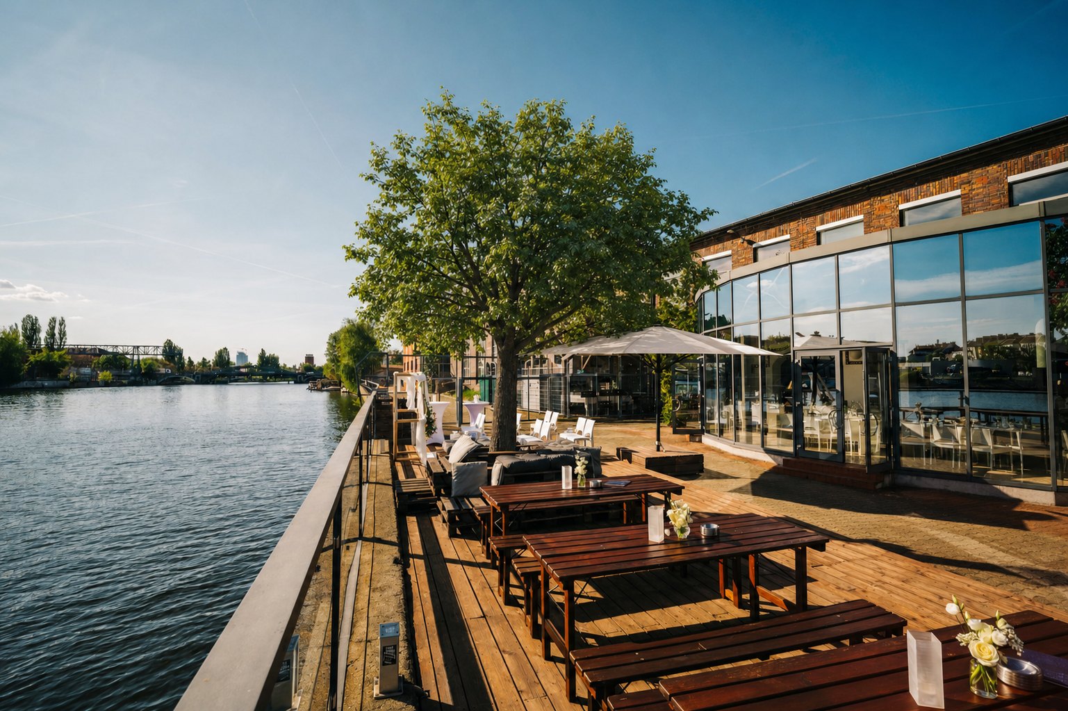 Holzterrasse der WHITE Spreelounge direkt an der Spree mit Sitzbänken, Baum und verglaster Panoramalounge