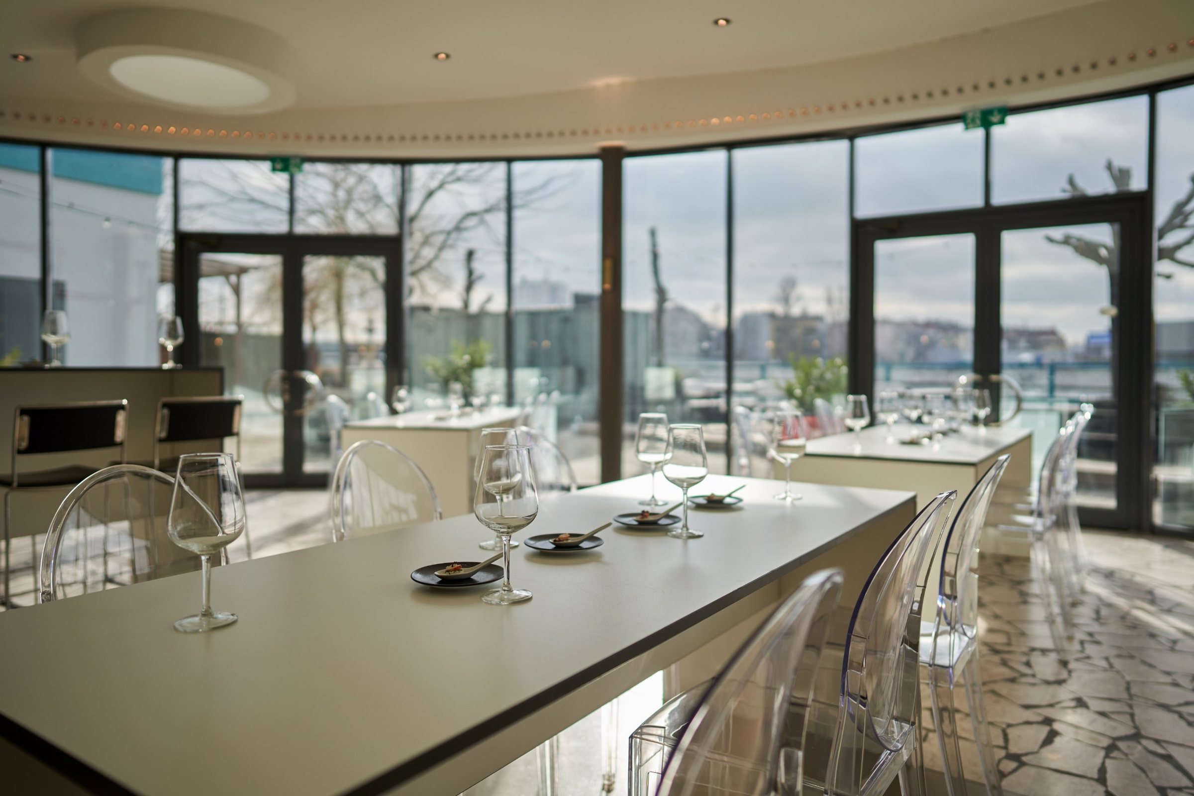 Panoramalounge mit Stehtischen, transparenten Stühlen und Fingerfood vor der Glasfront