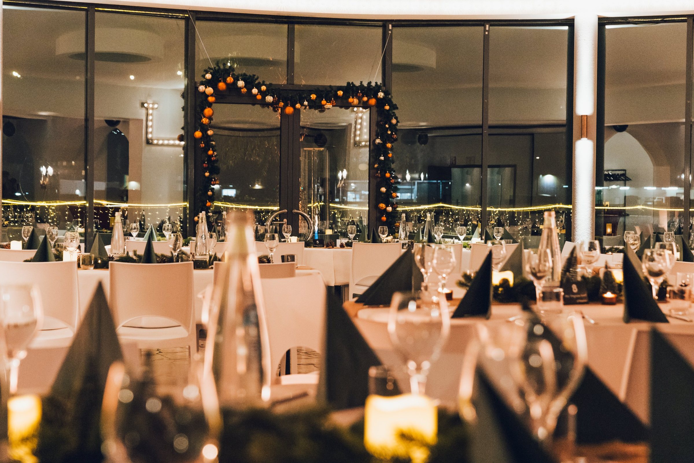 Weihnachtlich gedeckte Tische mit Kerzen und Tannengrün in der WHITE Spreelounge am Abend
