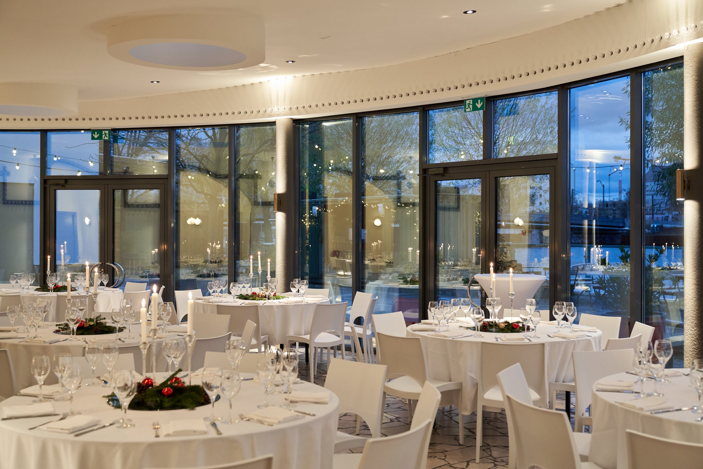Panoramalounge mit eingedeckten runden Tischen und Kerzen vor der Glasfront in der Dämmerung