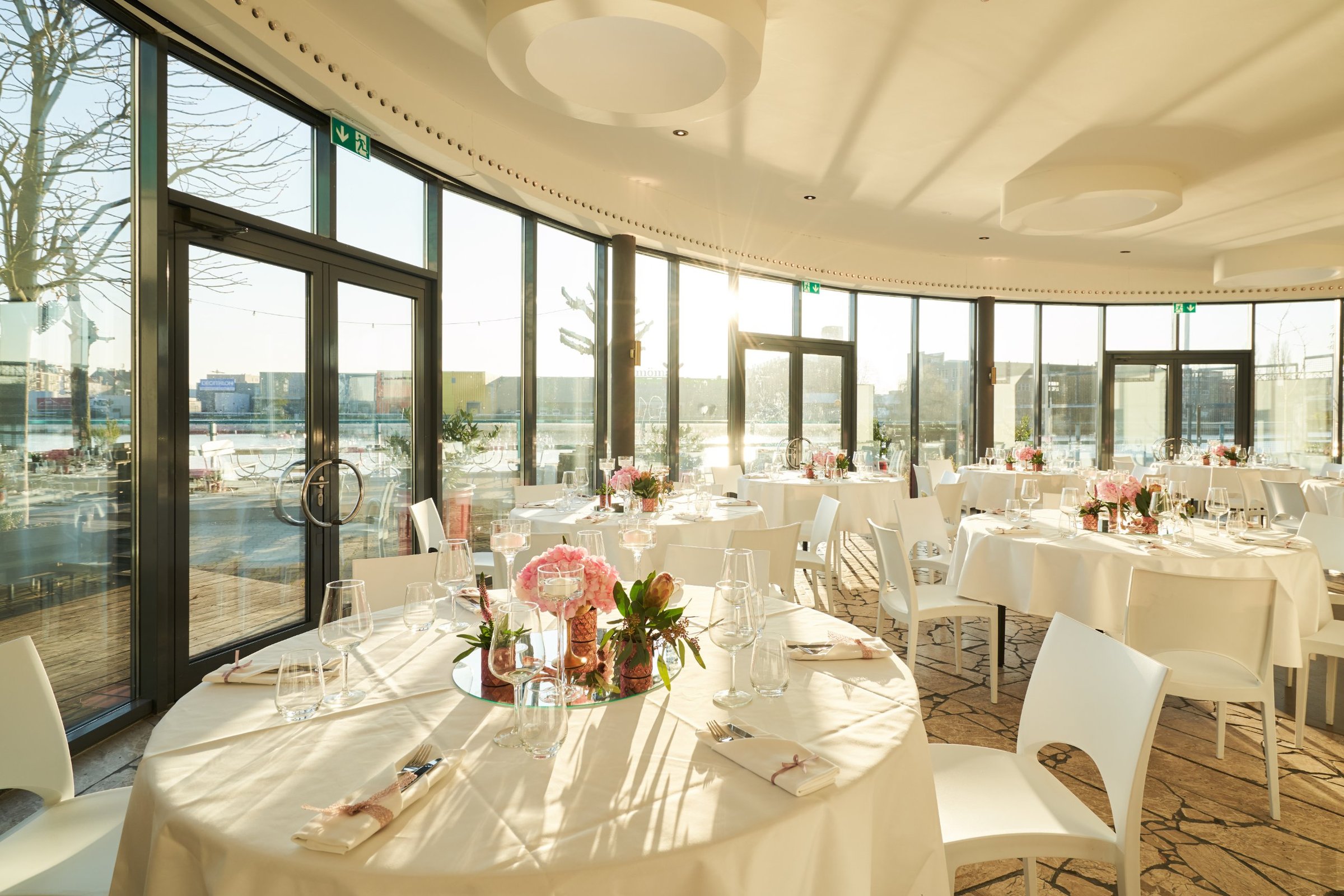 Panoramalounge der WHITE Spreelounge im Sonnenlicht mit runder Glasfront und festlich gedeckten Tischen