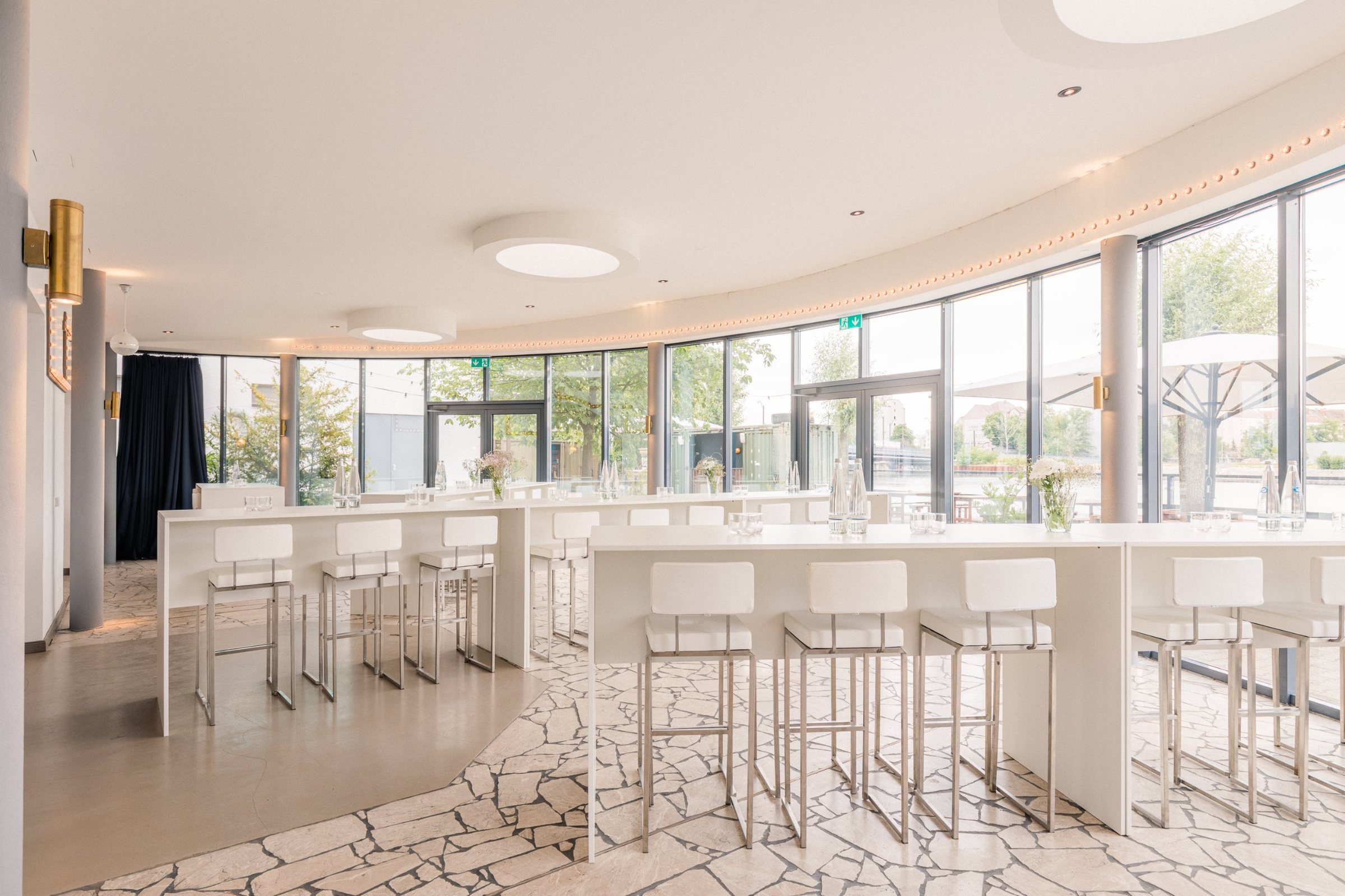 Panoramalounge mit weißen Hochtischen und Barhockern vor der runden Glasfront mit Blick auf die Spree