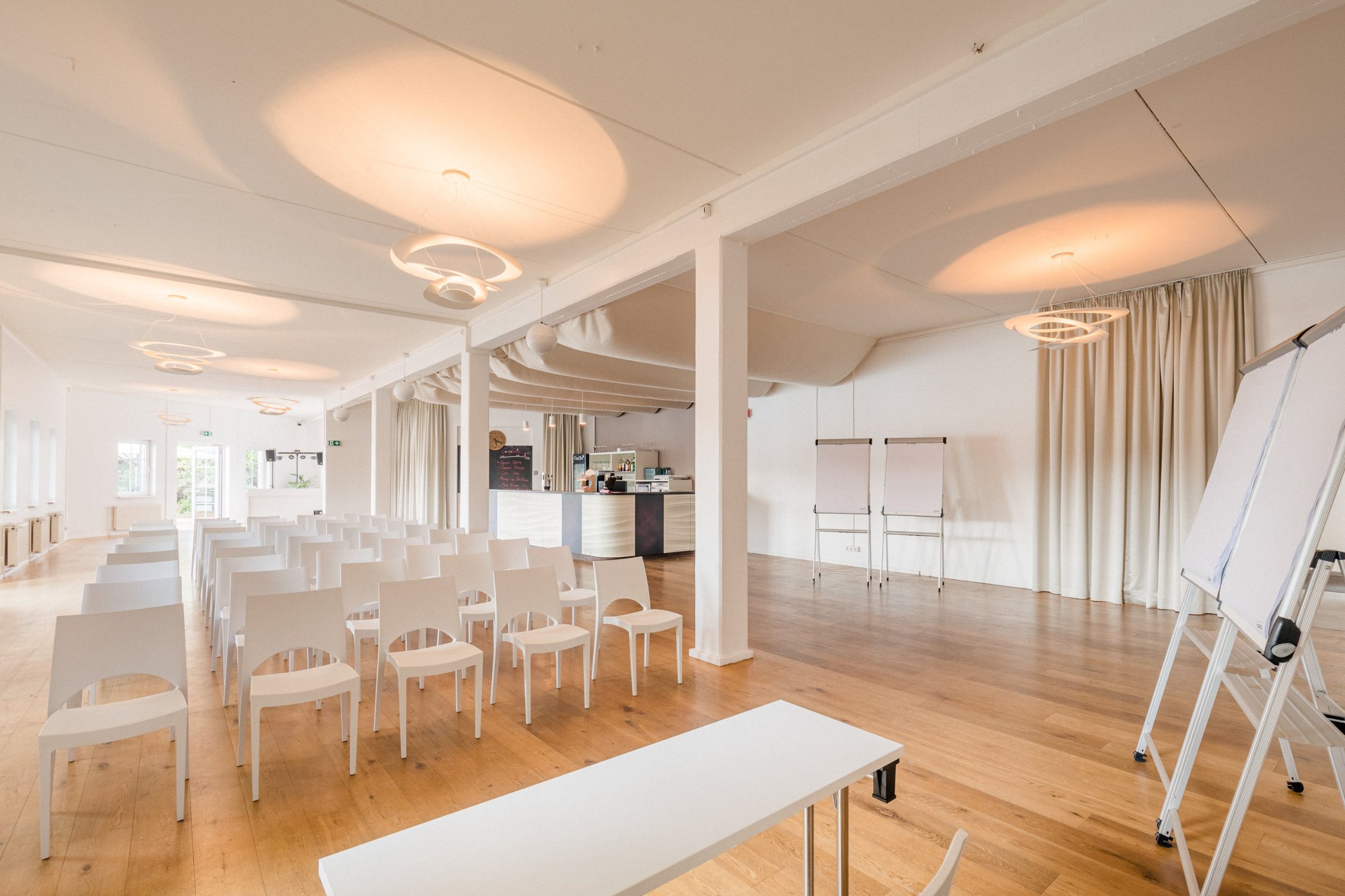 Heller Tagungsraum mit Reihenbestuhlung, Flipcharts und Bar in der WHITE Spreelounge