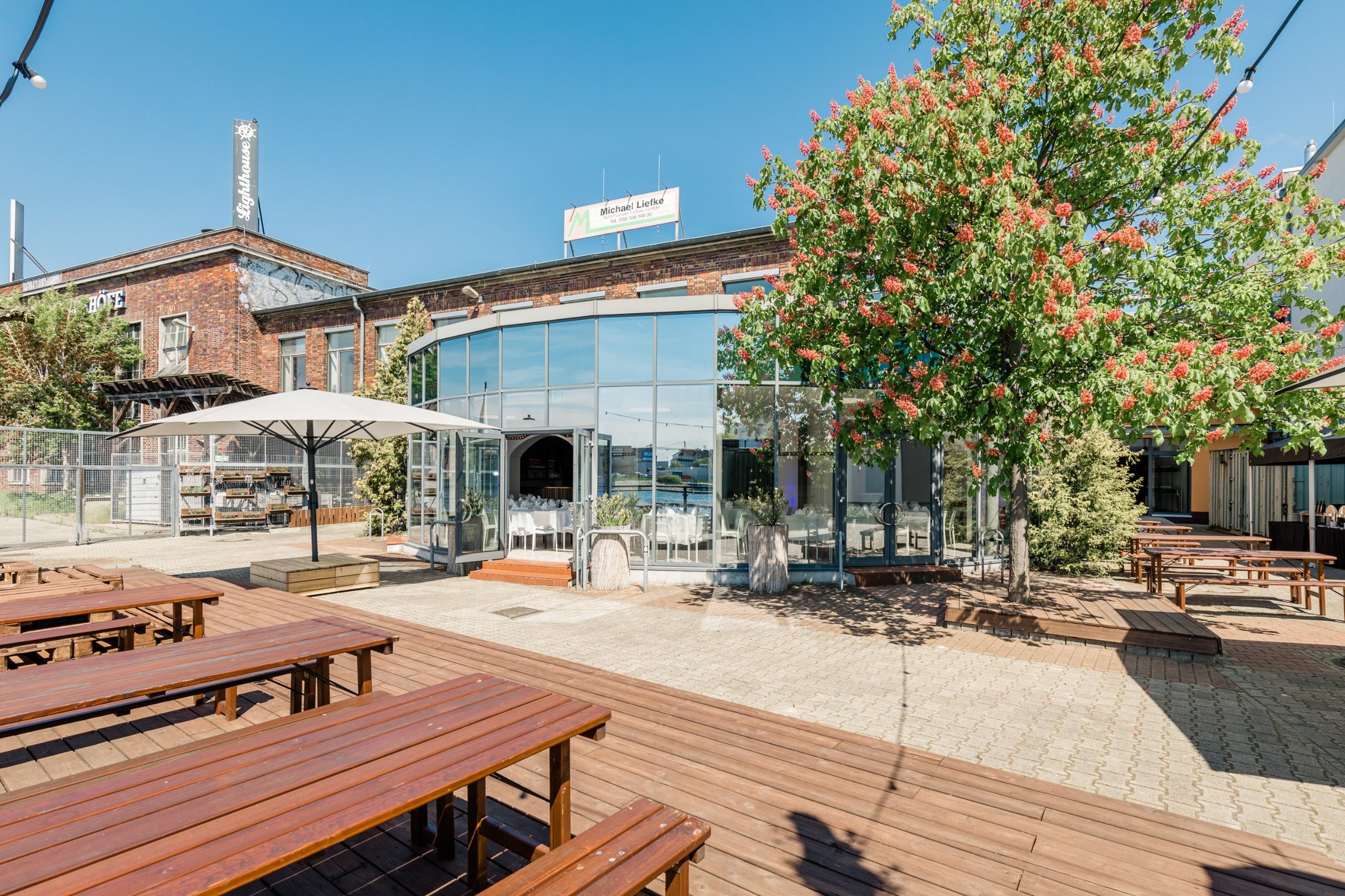 Lighthouse der WHITE Spreelounge von außen mit Glasfront, blühendem Kastanienbaum und Holzterrasse